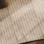 Area rug in a subtle stripe pattern in taupe, with a hint of a velvet chair leg. 