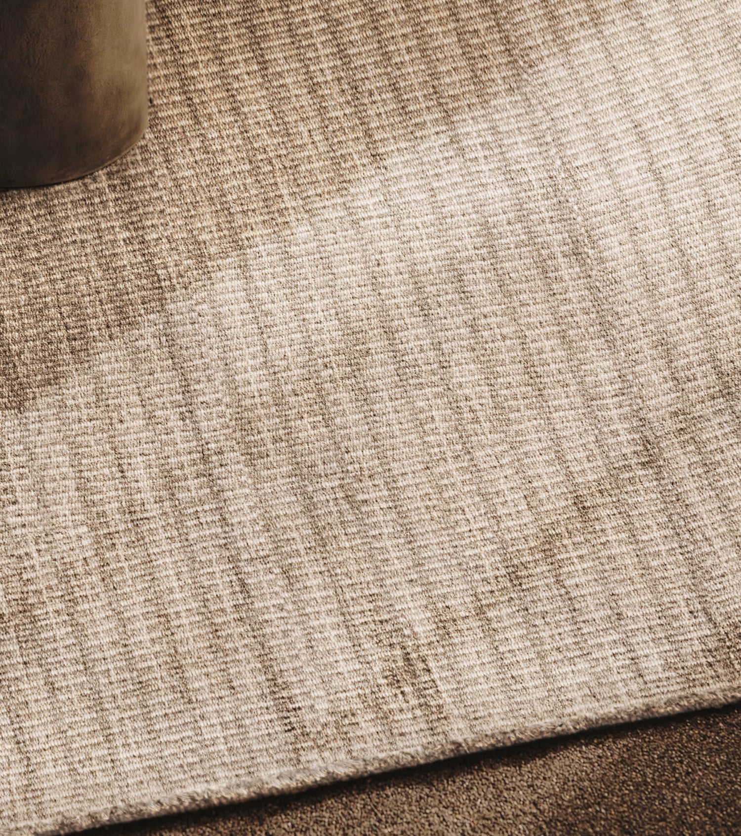Area rug in a subtle stripe pattern in taupe, with a hint of a velvet chair leg. 