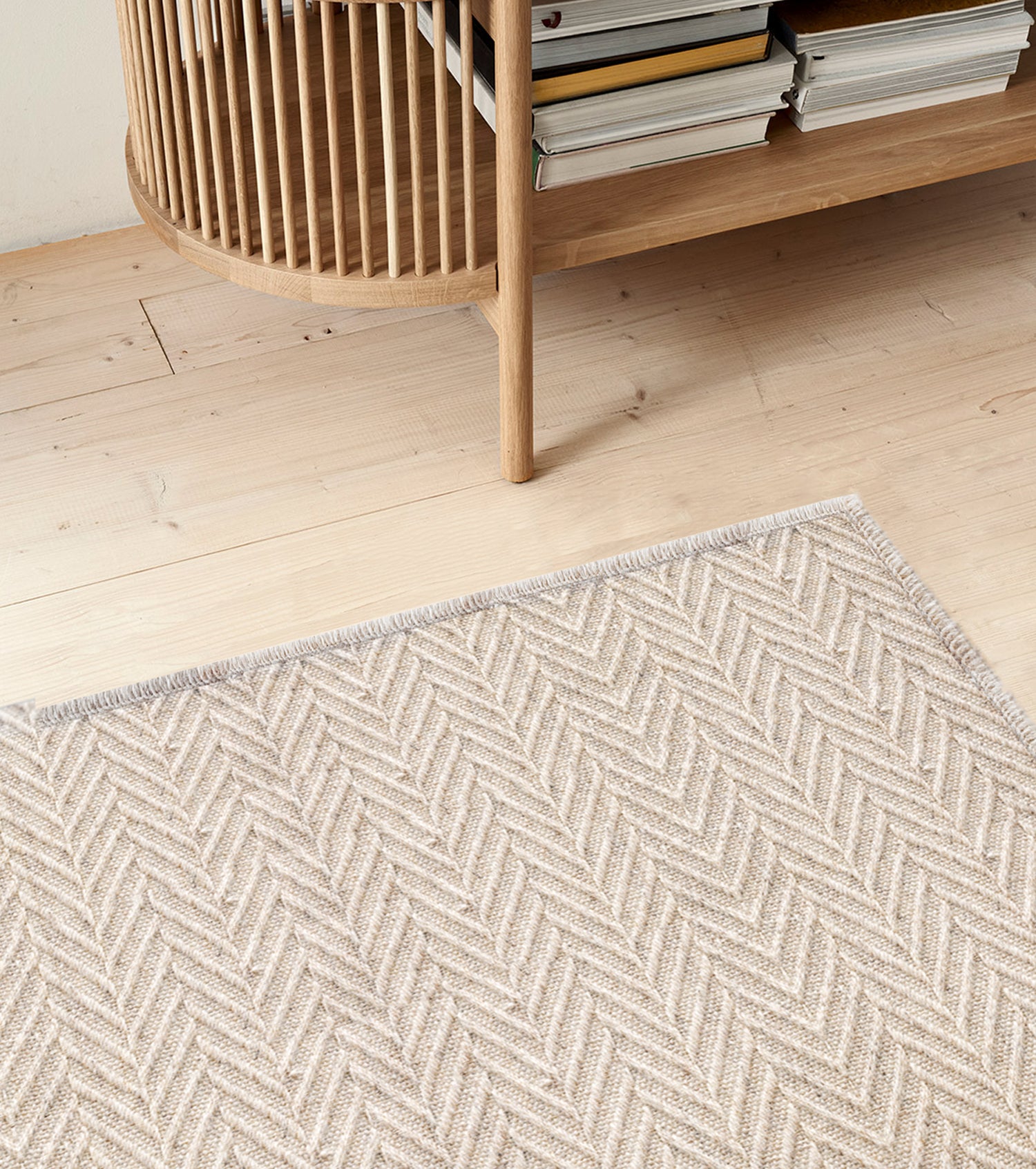 Herringbone patterned area rug in taupe on a wood floor with a bookshelf. 