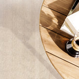 Round wooden table with books and coffee over carpet in a herringbone stripe in ecru.
