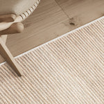 Detail shot of textural area rug on a wood floor with chair.