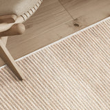 Detail shot of textural area rug on a wood floor with chair.