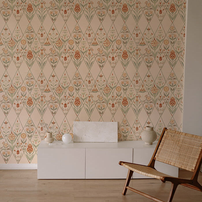 An armchair and credenza stand in front of a wall papered in a floral and diamond lattice print in green, orange and cream.
