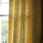 Yellow patterned curtain in front of a window with natural light.