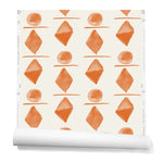 Partially unrolledwallpaper in a large-scale pattern of orange watercolored diamonds, circles and lines on a cream background. 