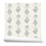 Partially unrolledwallpaper in a large-scale pattern of gray watercolored diamonds, circles and lines on a cream background. 