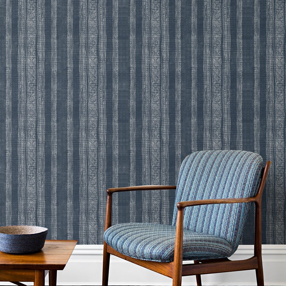 An armchair and coffee table in front of a wall papered in a striped pattern of intricate white lines over a washed denim background.