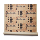 Partially unrolled wallpaper roll with layered geometric shapes in shades of black, beige and rust printed on a tan background.