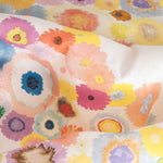Close up of fabric yardage in a painterly floral print in multicolor pastels on a white field.