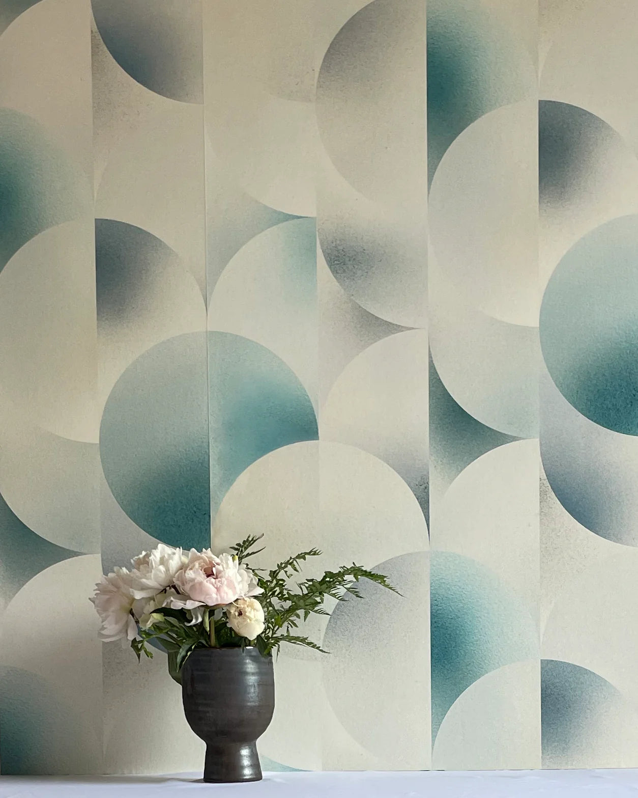 A vase of flowers stands in front of a wall covered in an abstract curvilinear print in mottled blue, gray and white.