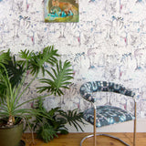 Modernist living tableau with a large plant and a statement wall papered in a painterly tree print.