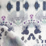 Draped fabric yardage in a watercolor inkblot print in shades of purple and gray on a cream field.