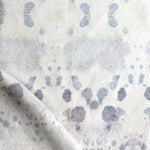 Draped fabric yardage in a watercolor inkblot print in shades of blue-gray on a cream field.