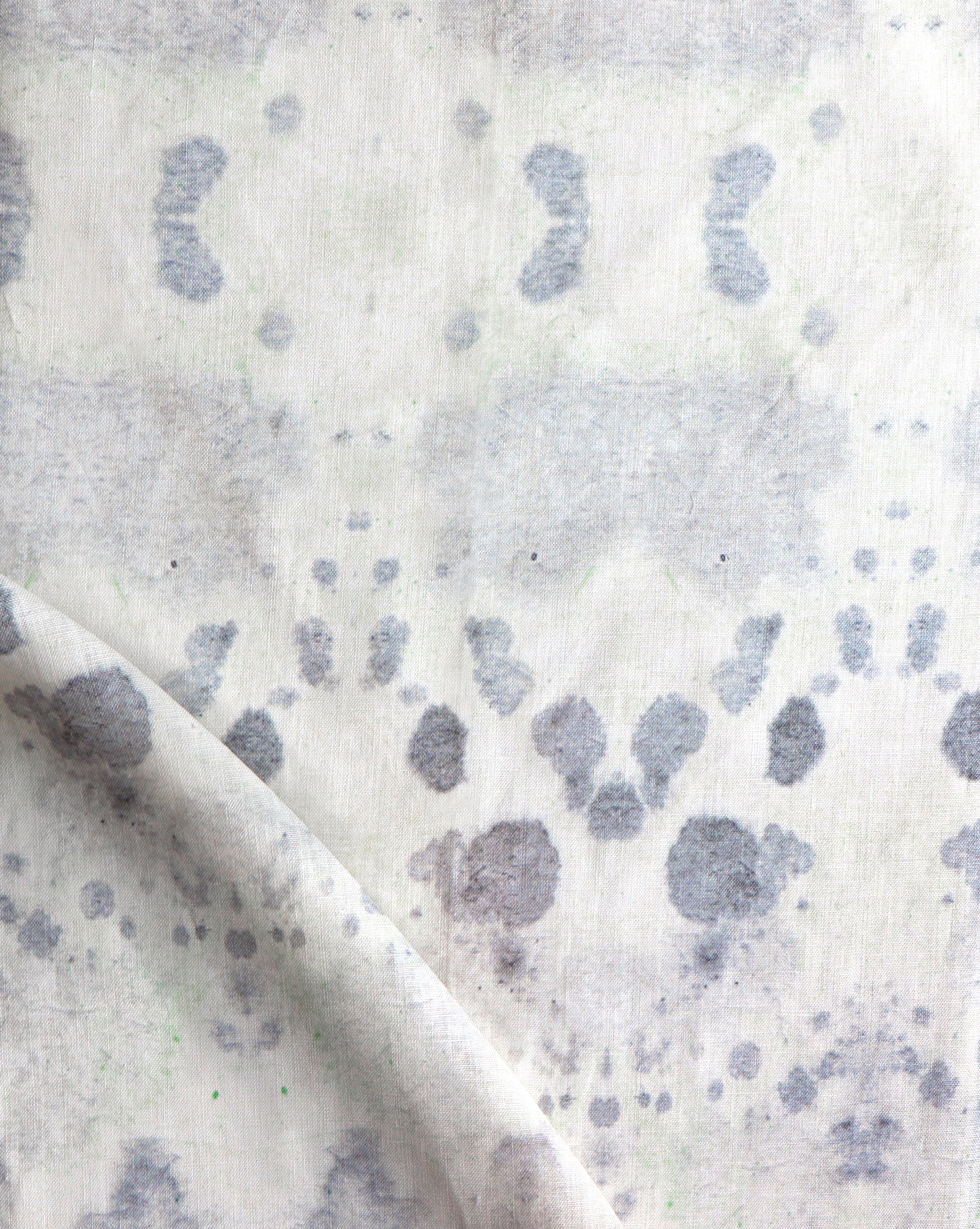 Draped fabric yardage in a watercolor inkblot print in shades of blue-gray on a cream field.