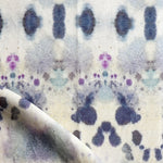 Draped fabric yardage in a watercolor inkblot print in shades of blue and purple on a cream field.