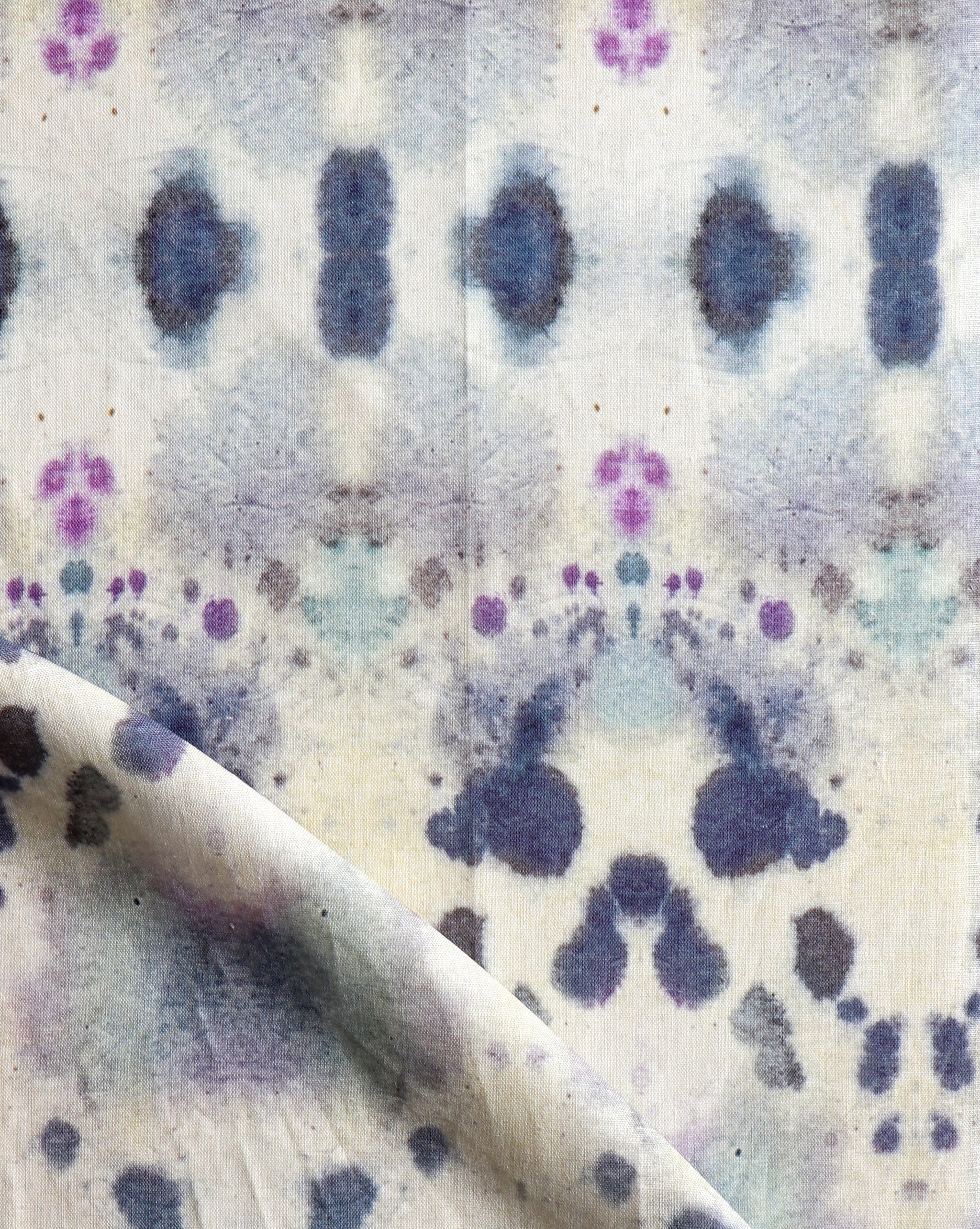 Draped fabric yardage in a watercolor inkblot print in shades of blue and purple on a cream field.