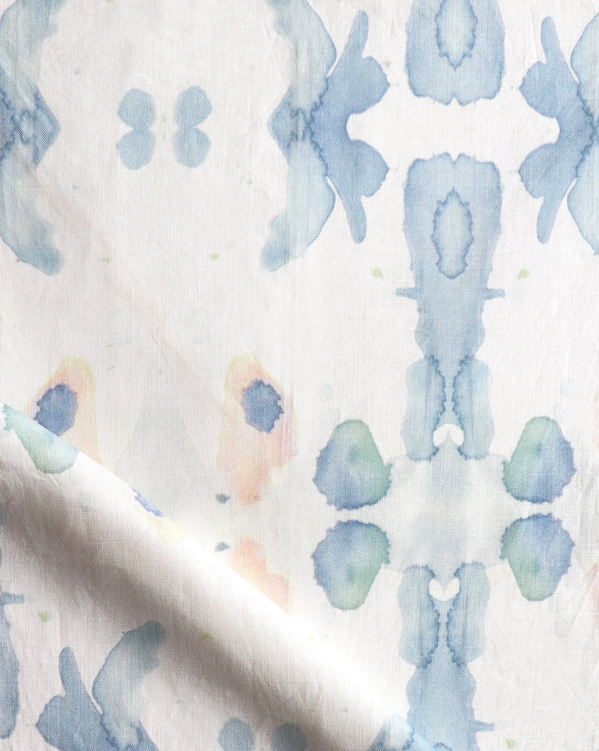 Draped fabric yardage in a watercolor ink splash print in shades of pastel blue and pink on a cream field.