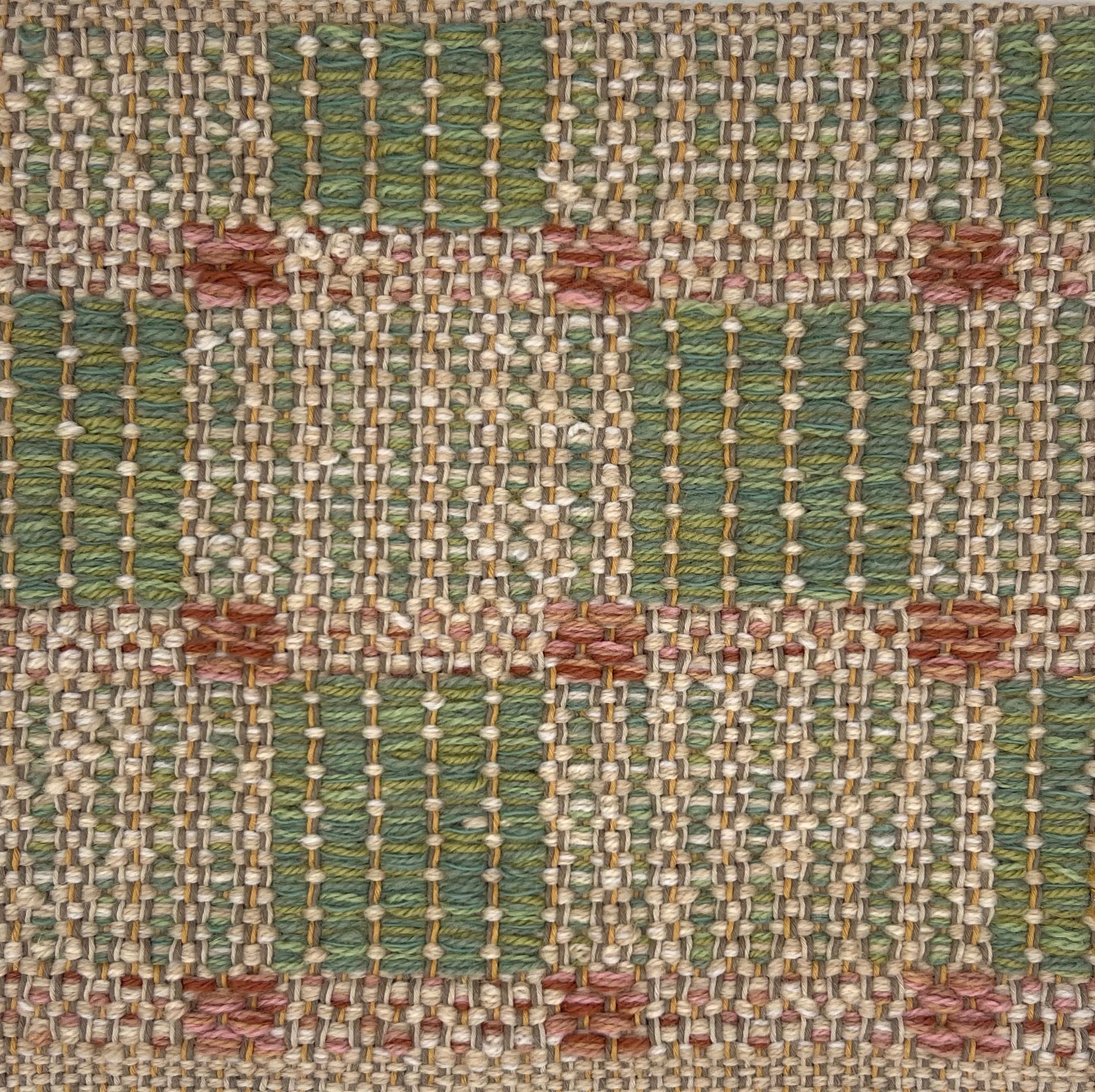 Textural flatweave rug in a checkerboard pattern in green and tan with blush pink accents.