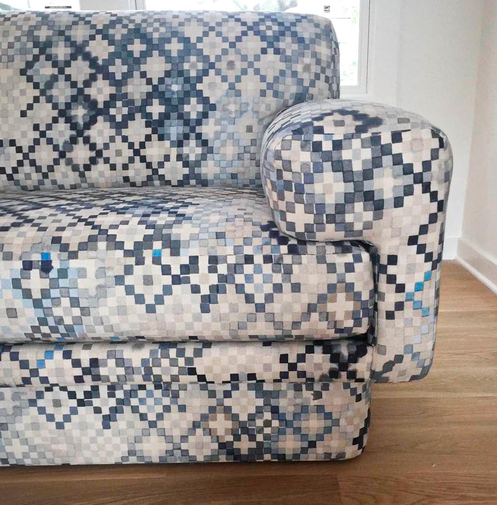 Detail of a sofa upholstered in a diamond checked pattern in shades of cream, gray and blue.
