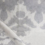 Draped fabric yardage in a watercolor ikat print in shades of gray on a greige field.