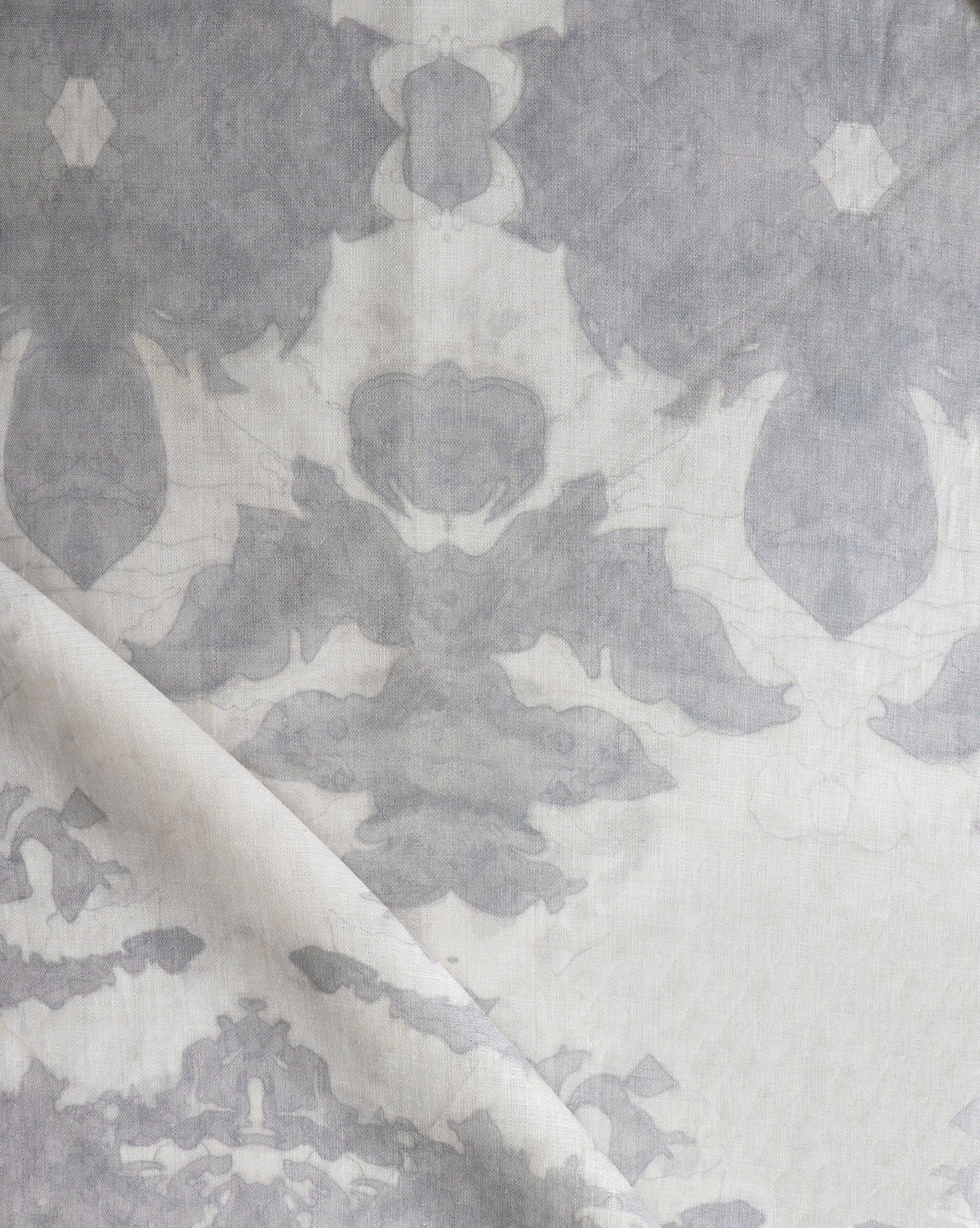 Draped fabric yardage in a watercolor ikat print in shades of gray on a greige field.