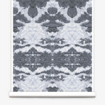 Partially unrolled wallpaper yardage in a painterly ikat print in shades of gray and light blue.