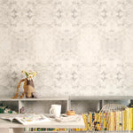 A cluttered desk and bookshelf stand in front of a wall papered in a watercolor textural print in cream, gray and tan.