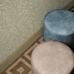Overhead image of two upholstered cylindrical ottomans in a dotted pattern in taupe and blue against a tan zebra wallpaper and geometric brown rug.