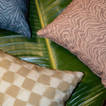 Styled flat-lay with detail of three throw pillows atop of a banana leaf with various patterns.