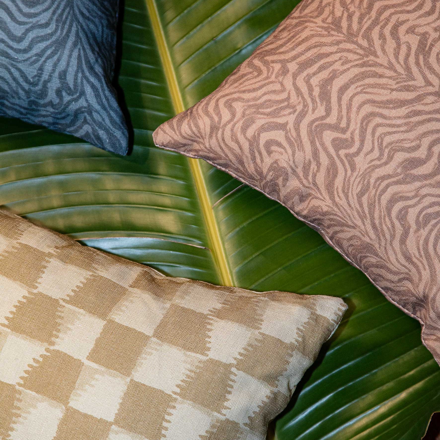 Styled flat-lay with detail of three throw pillows atop of a banana leaf with various patterns.