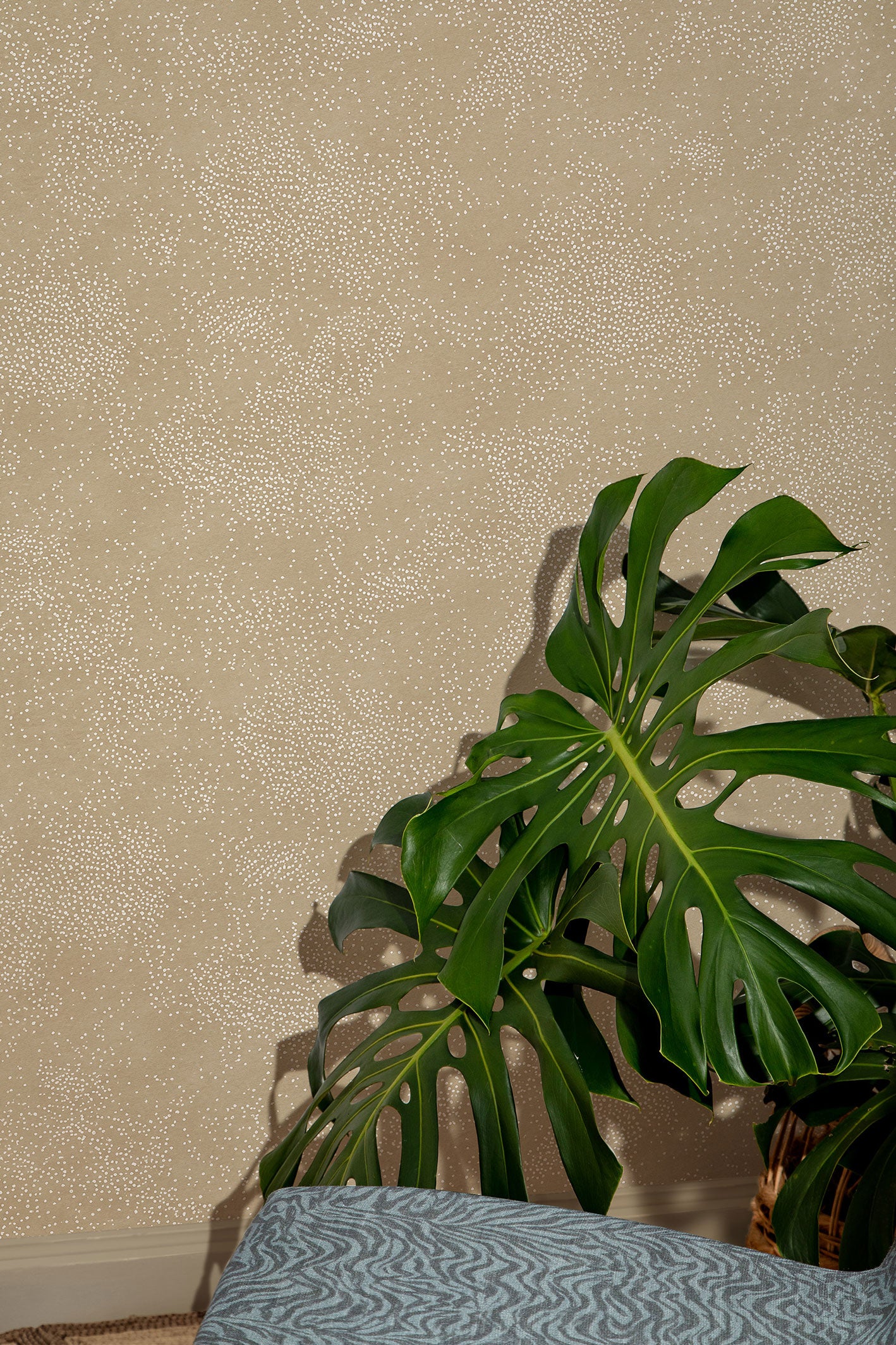 Cropped interior vignette detail with monstera leaves against a tan wallpaper with a dotted pattern and a blue zebra patterned chair seat at the foreground. 