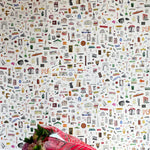 A bouquet of flowers lays in front of a wall papered in a playful illustrated "stuff" print in multicolor on a white field.