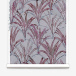 Partially unrolled wallpaper yardage in a painterly palm tree pattern in shades of purple and navy on a gray field.
