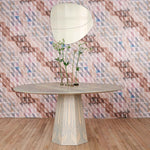 A modernist table with flowers stands in front of a wall papered in a painterly check pattern in brown, blue and pink.