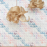 Two statement lamps hang in front of a wall papered in a painterly check pattern in shades of coral, purple, green and white.