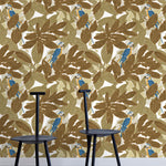 Two minimalist black chairs stand in front of a wall papered in a botanical and parrot print in bronze, brown, navy and yellow.
