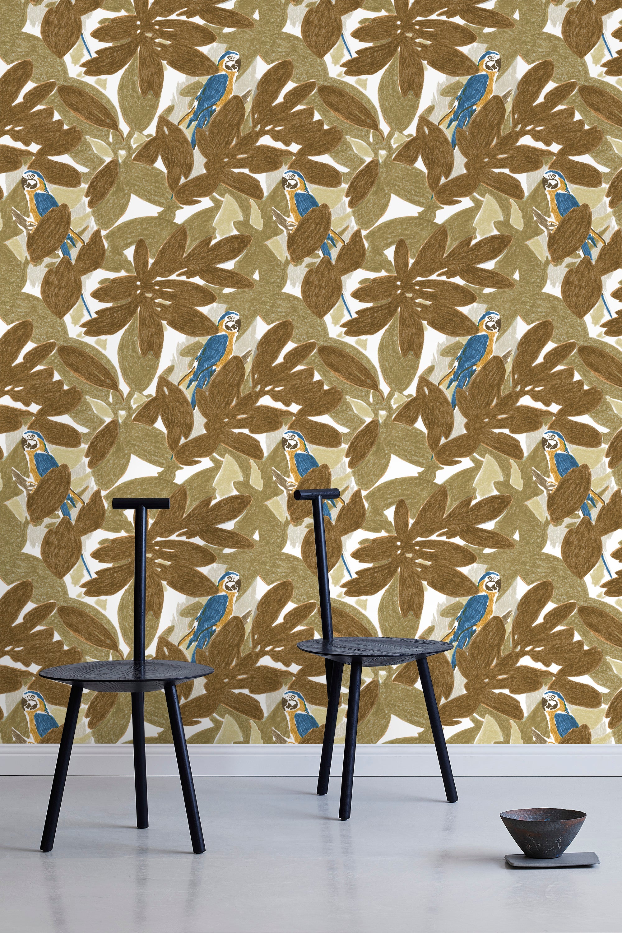 Two minimalist black chairs stand in front of a wall papered in a botanical and parrot print in bronze, brown, navy and yellow.