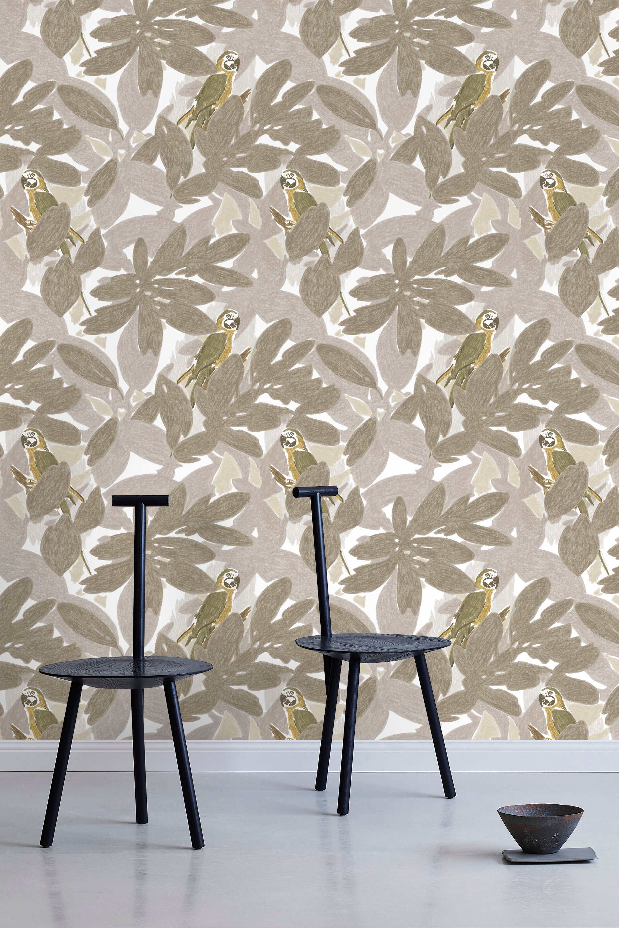 Two minimalist black chairs stand in front of a wall papered in a botanical and parrot print in gray, brown and yellow.