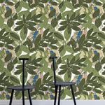 Two minimalist black chairs stand in front of a wall papered in a botanical and parrot print in green, blue and yellow.
