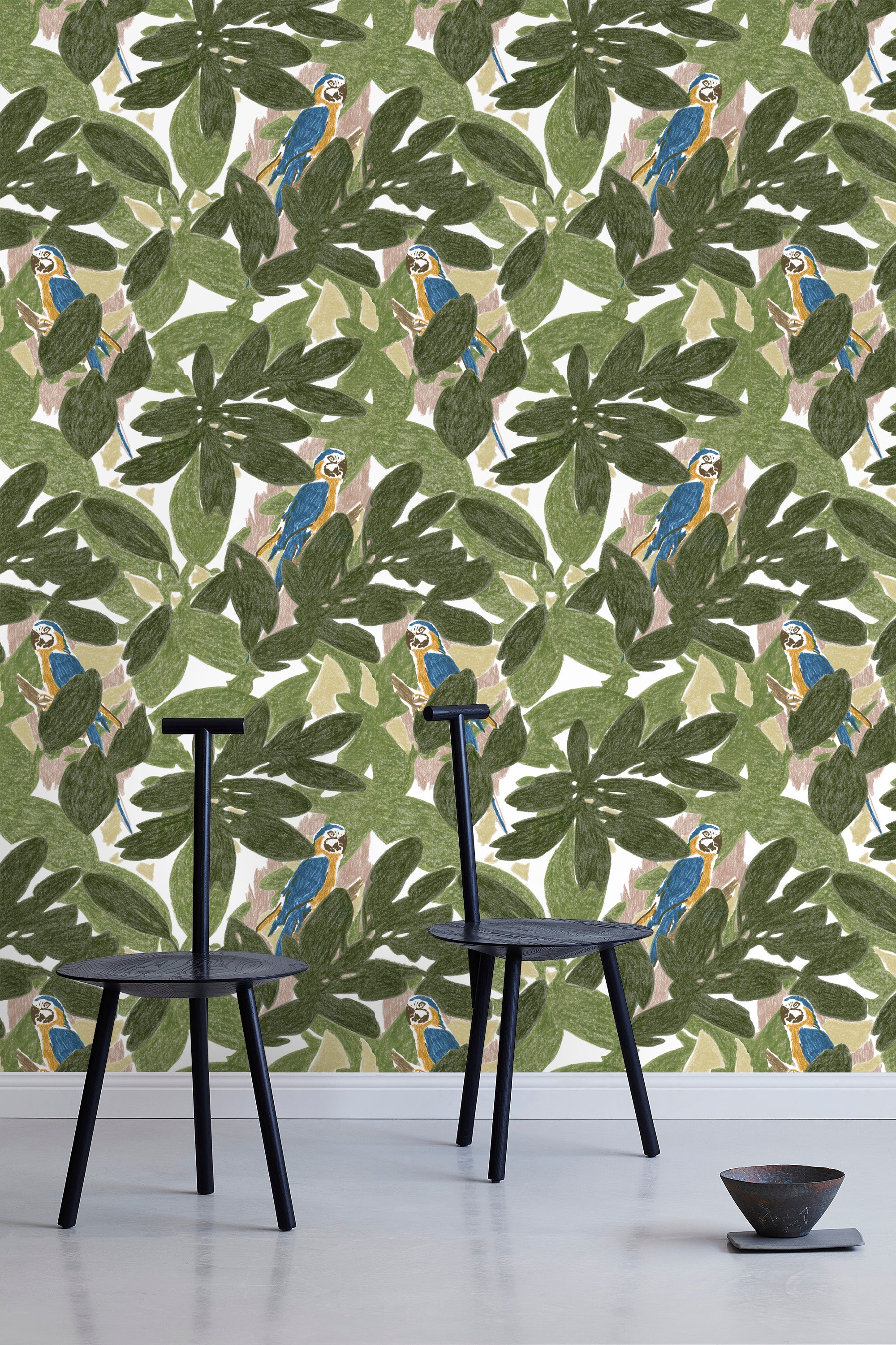 Two minimalist black chairs stand in front of a wall papered in a botanical and parrot print in green, blue and yellow.