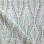 Draped fabric yardage in a watercolor diamond print in shades of gray and blue on a cream field.