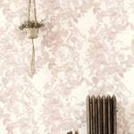 A living space with a radiator, a plant and a wall papered in a watercolor floral print in mottled pink, gray and white.