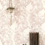A living space with a radiator, a plant and a wall papered in a watercolor floral print in mottled pink, gray and white.