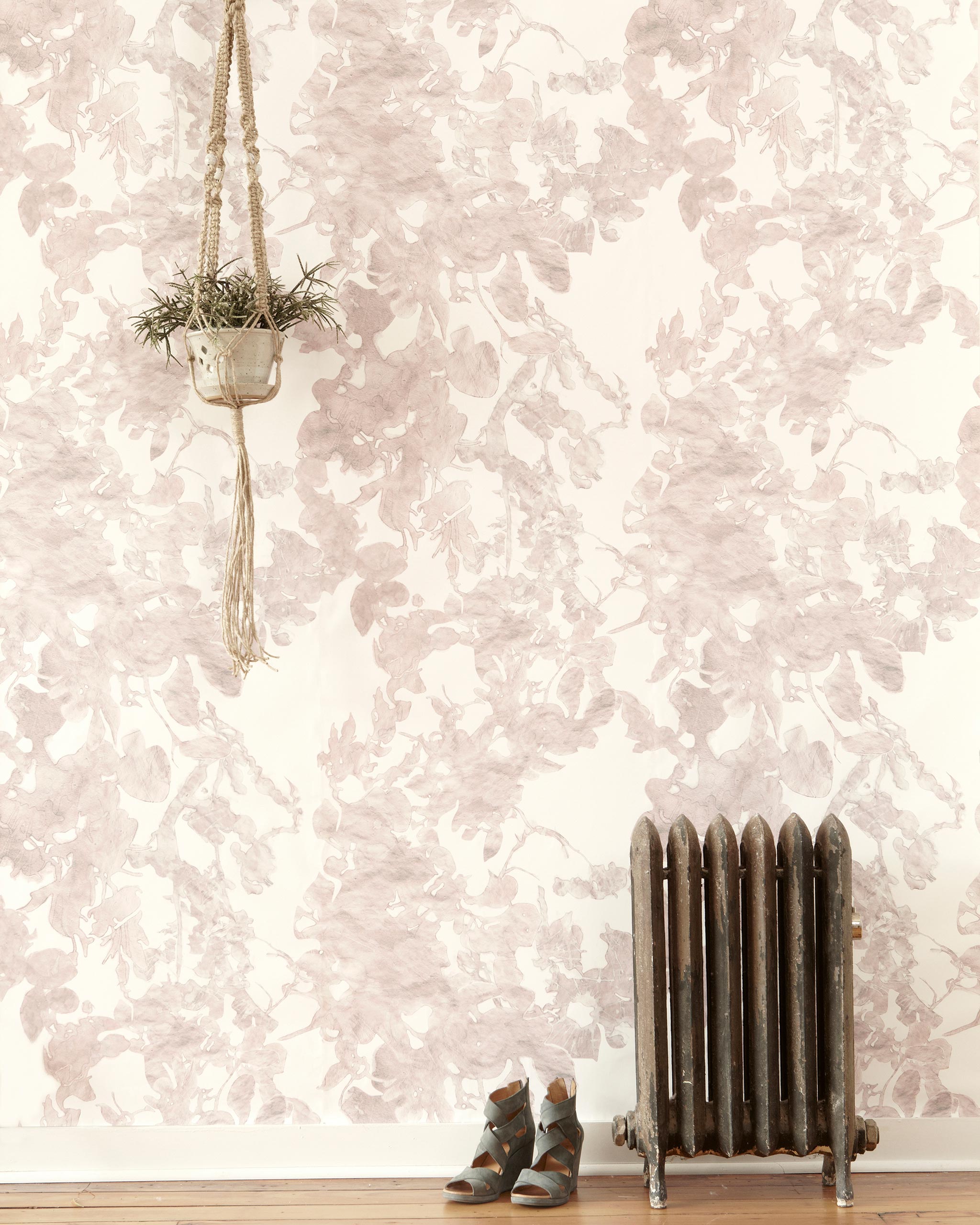 A living space with a radiator, a plant and a wall papered in a watercolor floral print in mottled pink, gray and white.