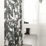 A bathroom with black and white subway tiles and a shower curtain in a watercolor black and white tree print.