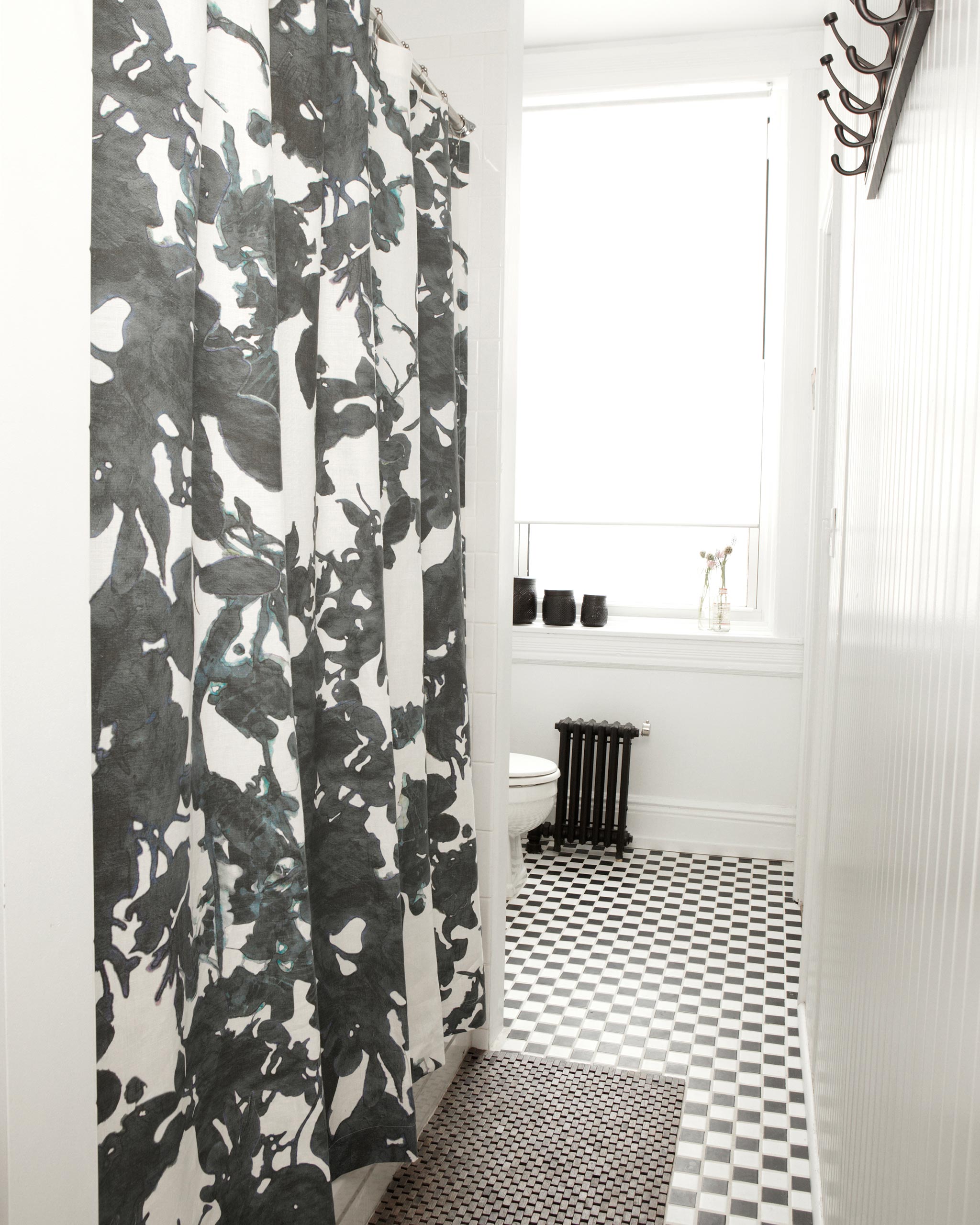 A bathroom with black and white subway tiles and a shower curtain in a watercolor black and white tree print.