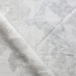 Draped fabric yardage in a watercolor tree print in shades of gray on a cream field.