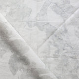 Draped fabric yardage in a watercolor tree print in shades of gray on a cream field.