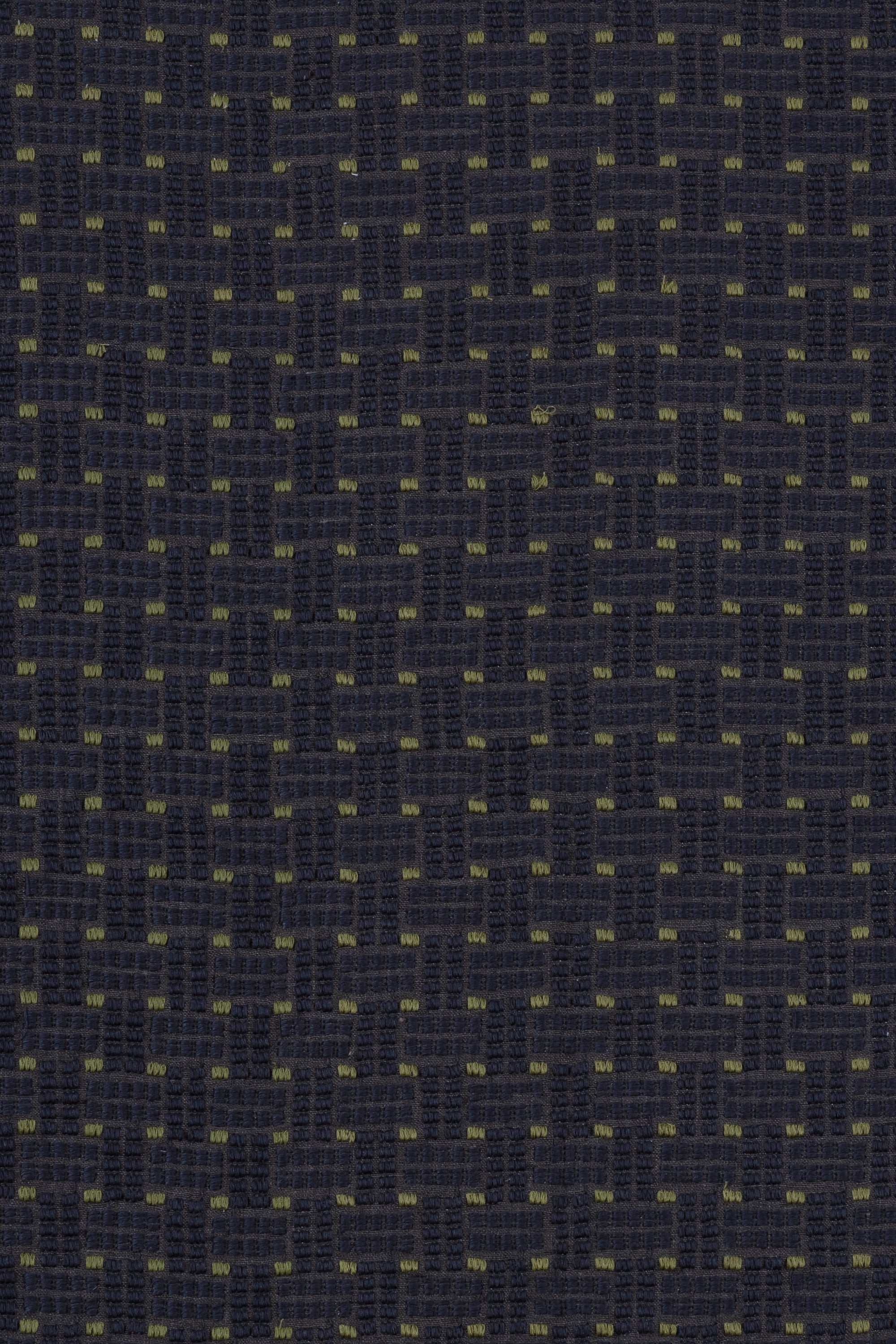 Detail of an embroidered fabric in a dashed basketweave design in navy blue with green accents.