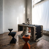Marble pedestal console table with black and tan flame bordered runner with a bust, framed by sculptural side stools.